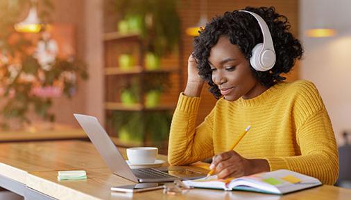 微笑的黑人女孩带着无线耳机在线学习，在咖啡馆使用笔记本电脑，做笔记